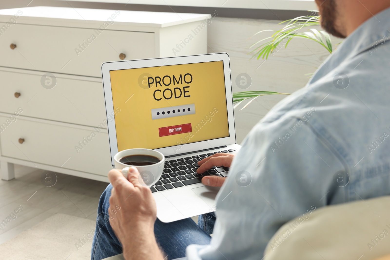 Photo of Man holding laptop with activated promo code and cup of coffee indoors, closeup