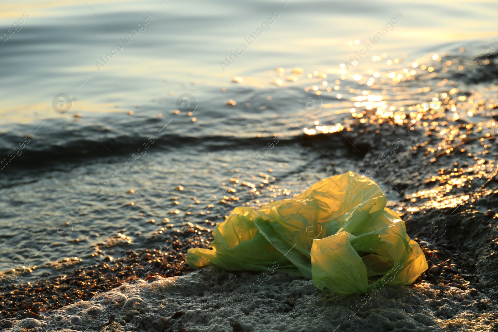 Photo of Used plastic bag near water at beach, space for text. Environment pollution