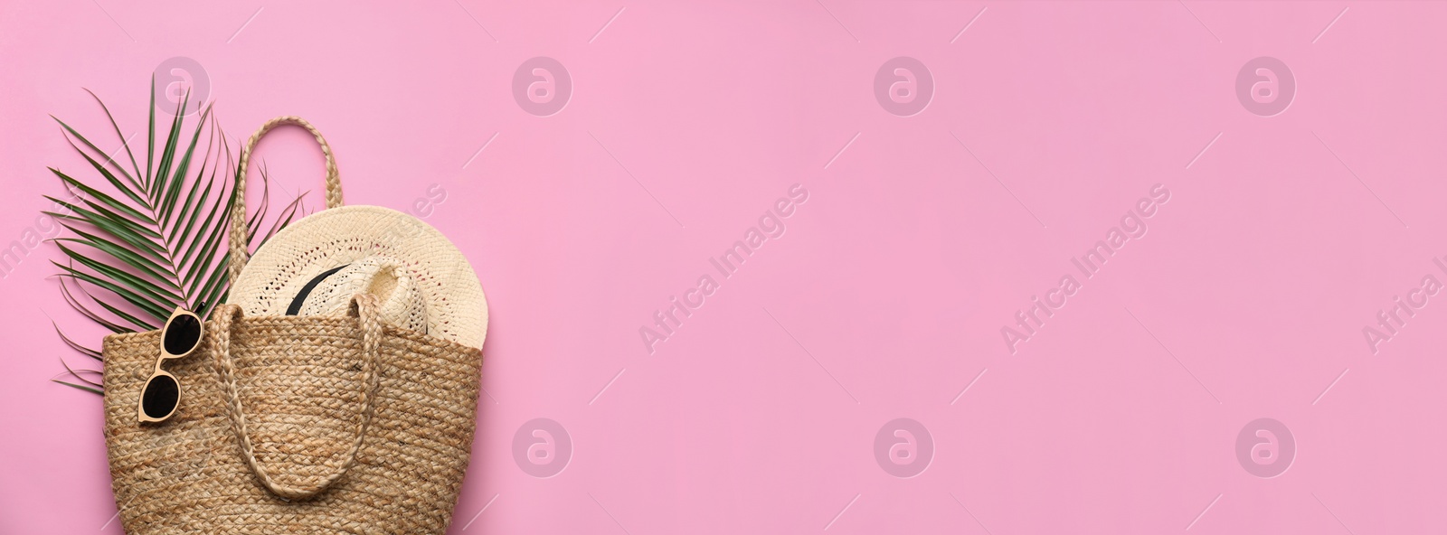 Photo of Elegant woman's straw bag with hat, tropical leaf and sunglasses on pink background, top view. Space for text