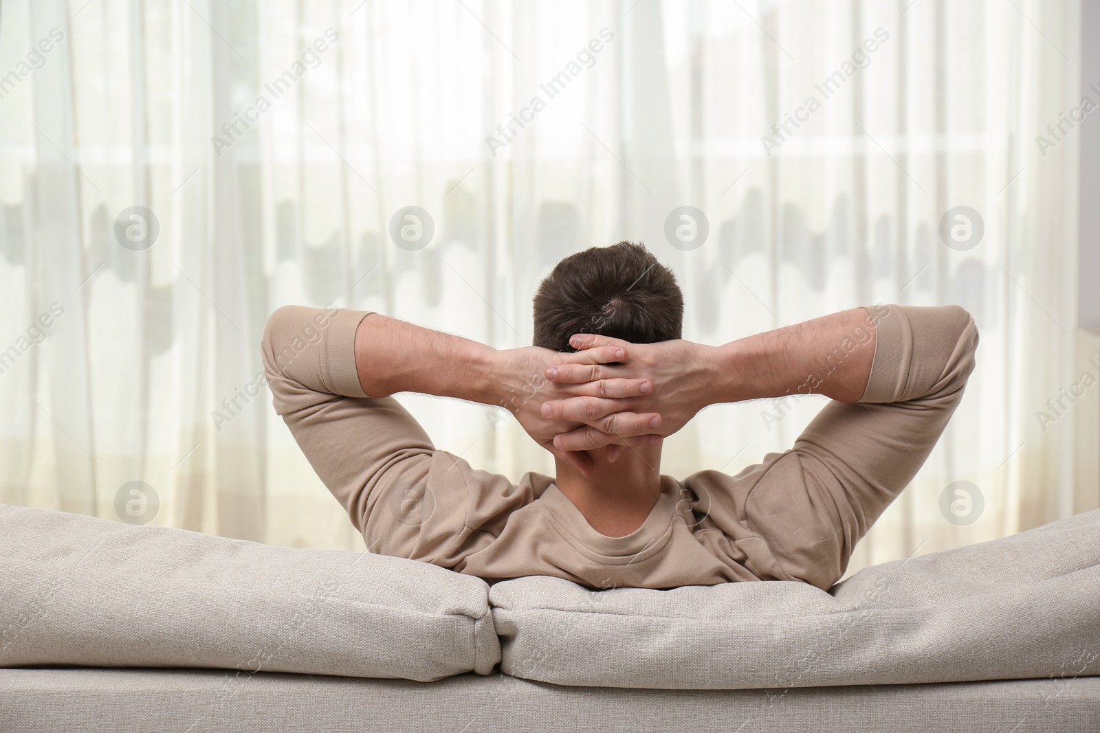 Photo of Man relaxing on sofa at home, back view