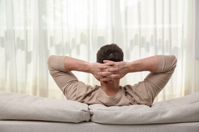 Photo of Man relaxing on sofa at home, back view