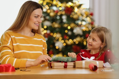 Photo of Christmas presents wrapping. Mother and her little daughter decorating gift box with fir tree branch at home