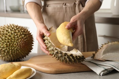 Woman peeling durian at table in kitchen, closeup