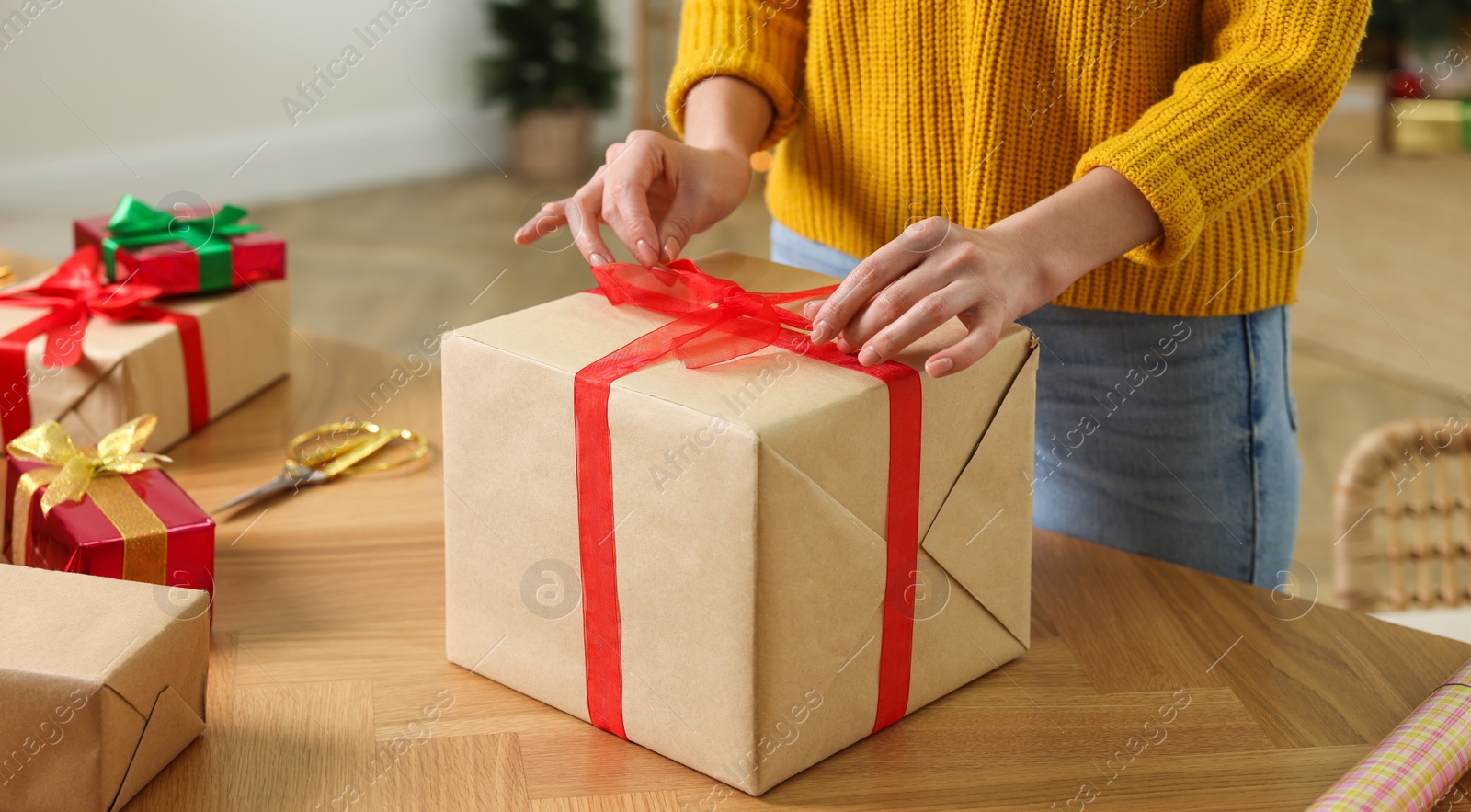 Photo of Woman wrapping Christmas gift at wooden table indoors, closeup