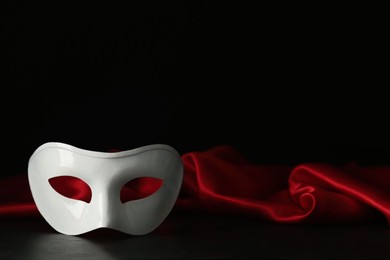 Photo of White theatre mask and red fabric on black background, space for text