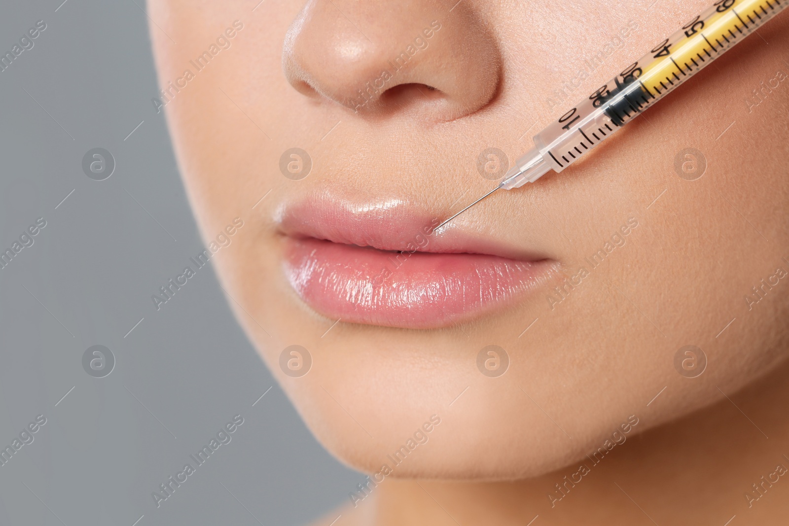 Photo of Young woman getting lips injection on grey background, closeup. Cosmetic surgery