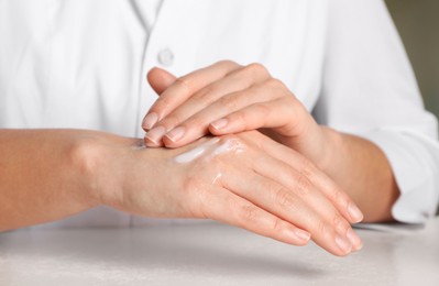 Photo of Dermatologist testing cosmetic product at white table, closeup