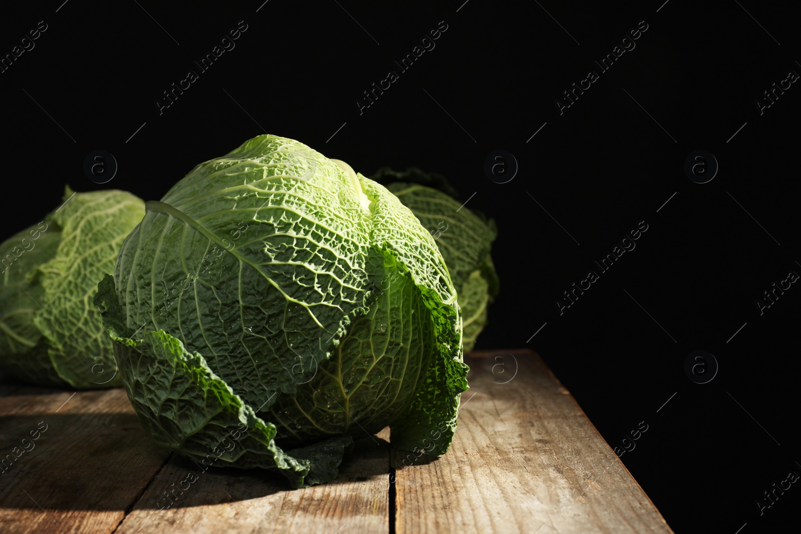 Photo of Savoy cabbage on wooden table against black background. Space for text