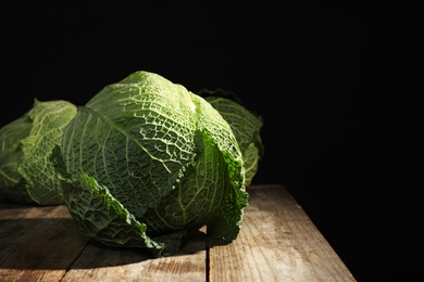 Savoy cabbage on wooden table against black background. Space for text