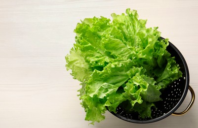 Fresh lettuce in black colander on white wooden table, top view. Space for text