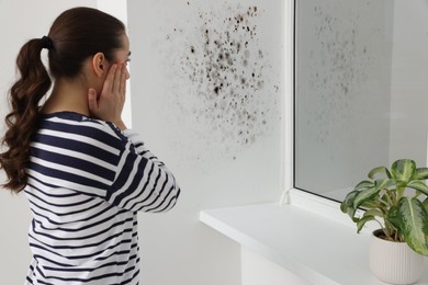 Image of Shocked woman looking at affected with mold window slope in room