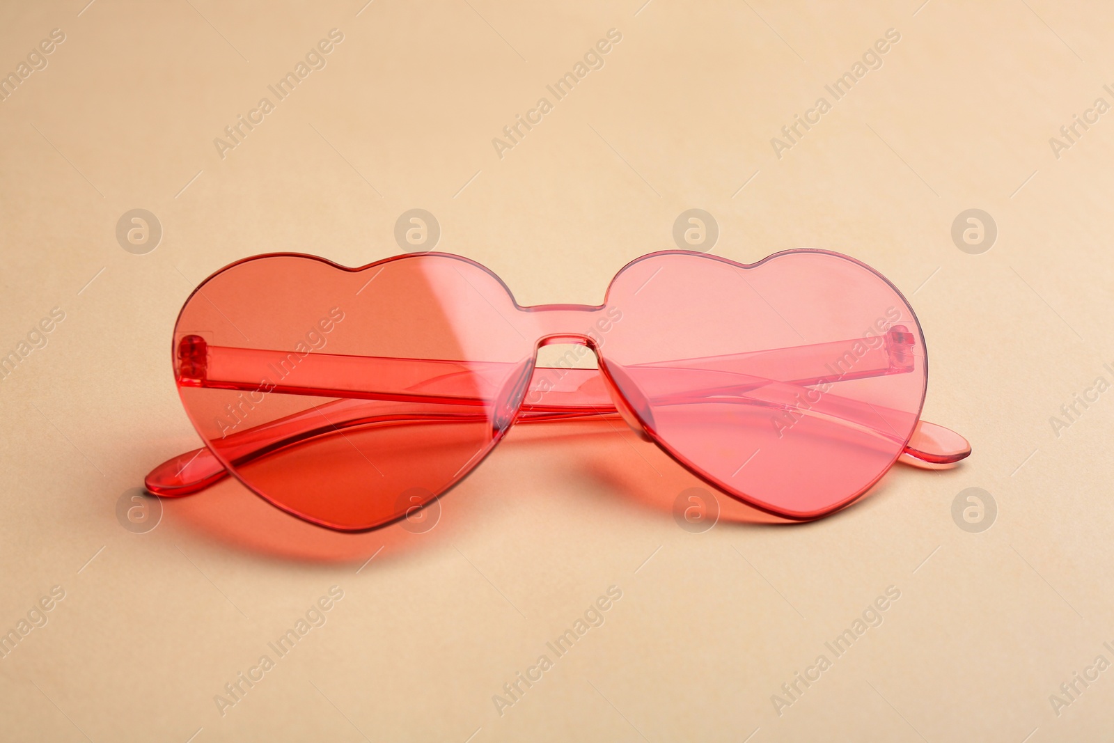 Photo of Stylish heart shaped sunglasses on beige background. Fashionable accessory