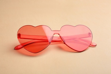 Photo of Stylish heart shaped sunglasses on beige background. Fashionable accessory