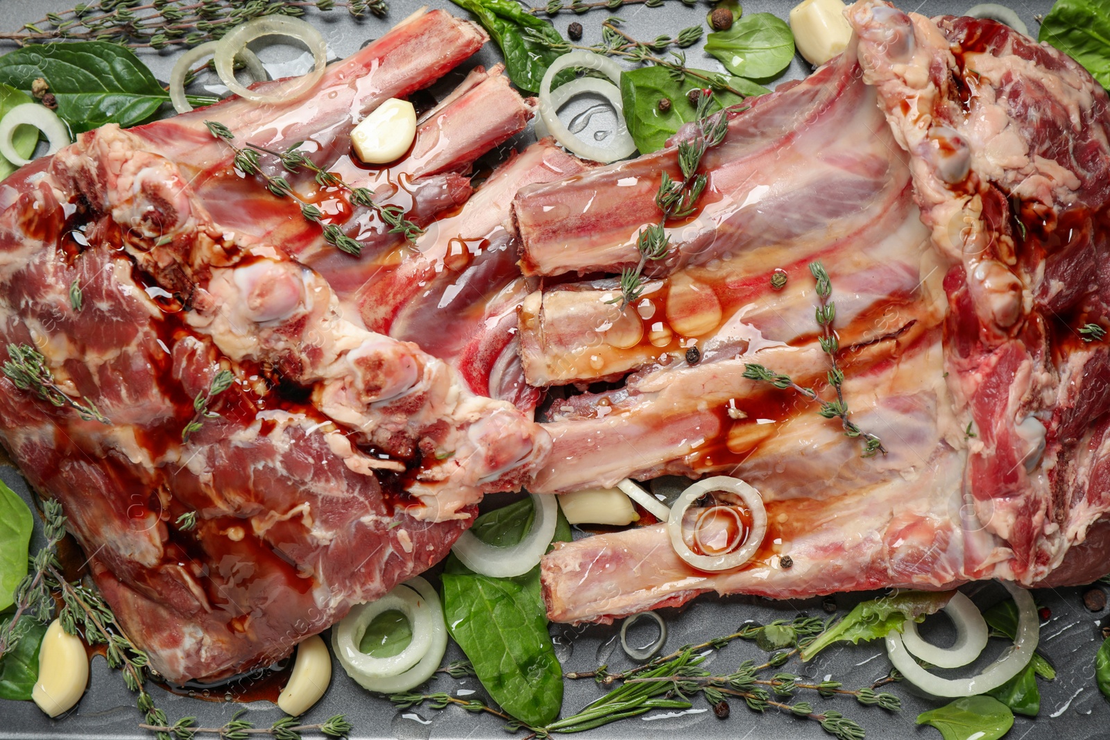 Photo of Raw spare ribs with herbs and seasonings on grey table, closeup