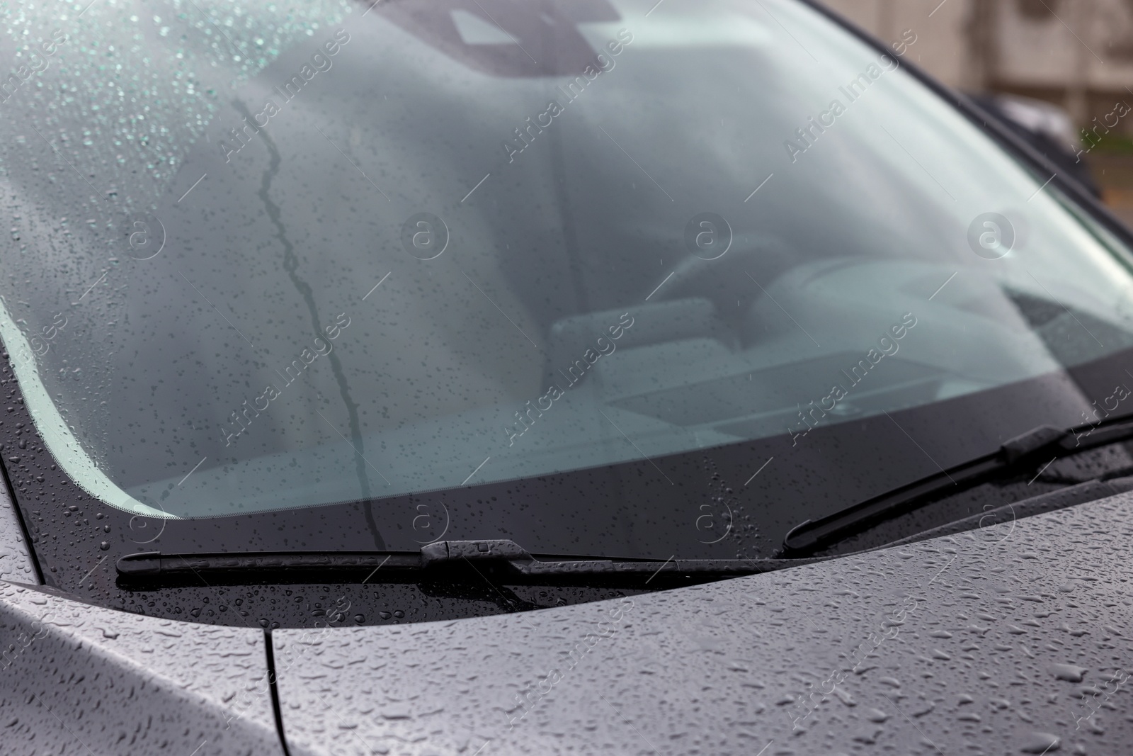 Photo of Car wipers cleaning water drops from windshield glass outdoors, closeup