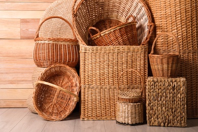 Photo of Many different wicker baskets made of natural material on floor near wooden wall