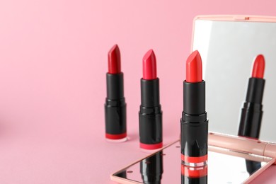 Photo of Different beautiful lipsticks and mirror on pink background, space for text