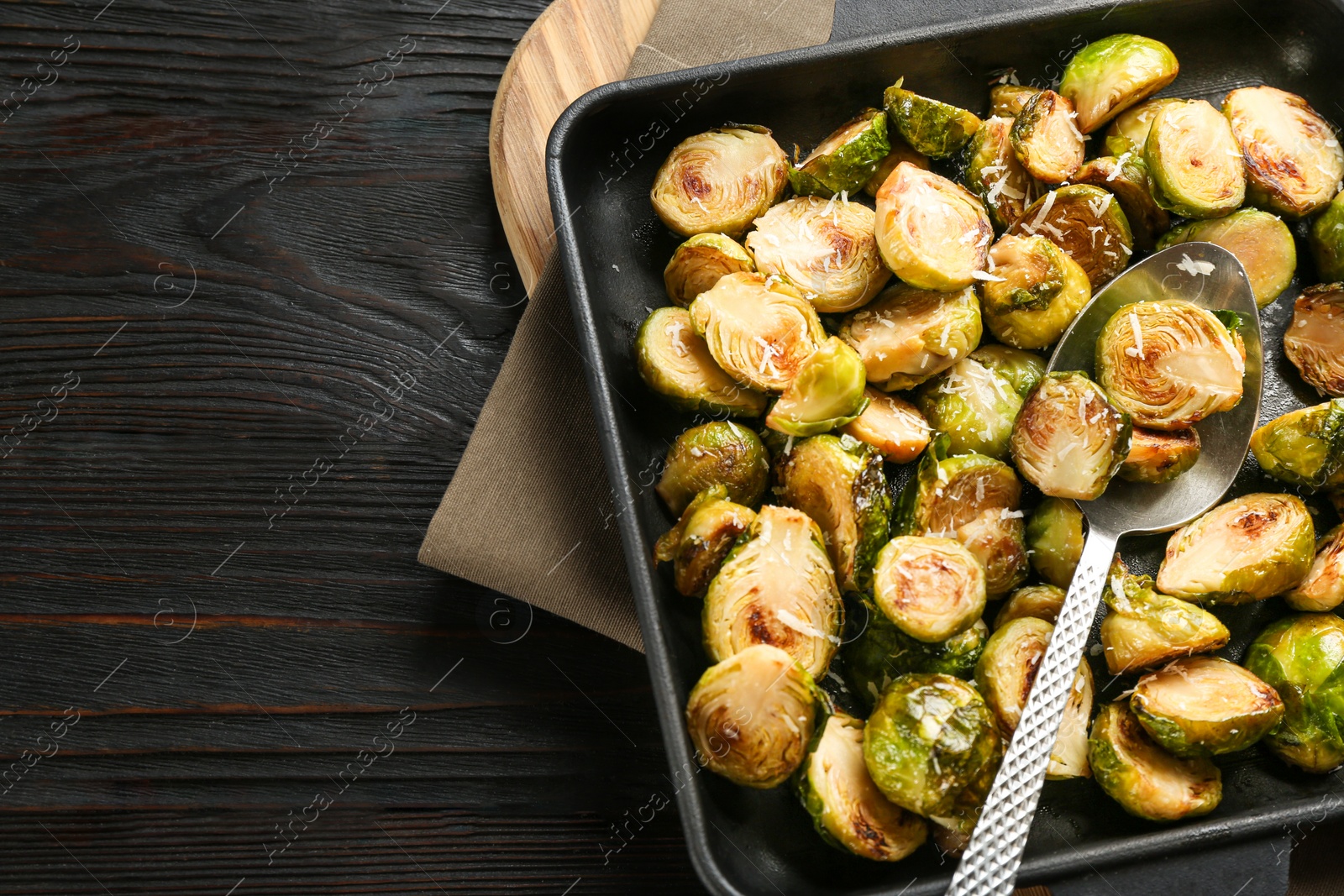 Photo of Delicious roasted brussels sprouts with grated cheese on black wooden table, top view. Space for text