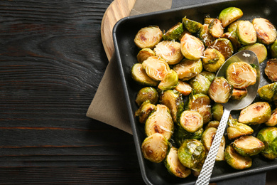 Photo of Delicious roasted brussels sprouts with grated cheese on black wooden table, top view. Space for text