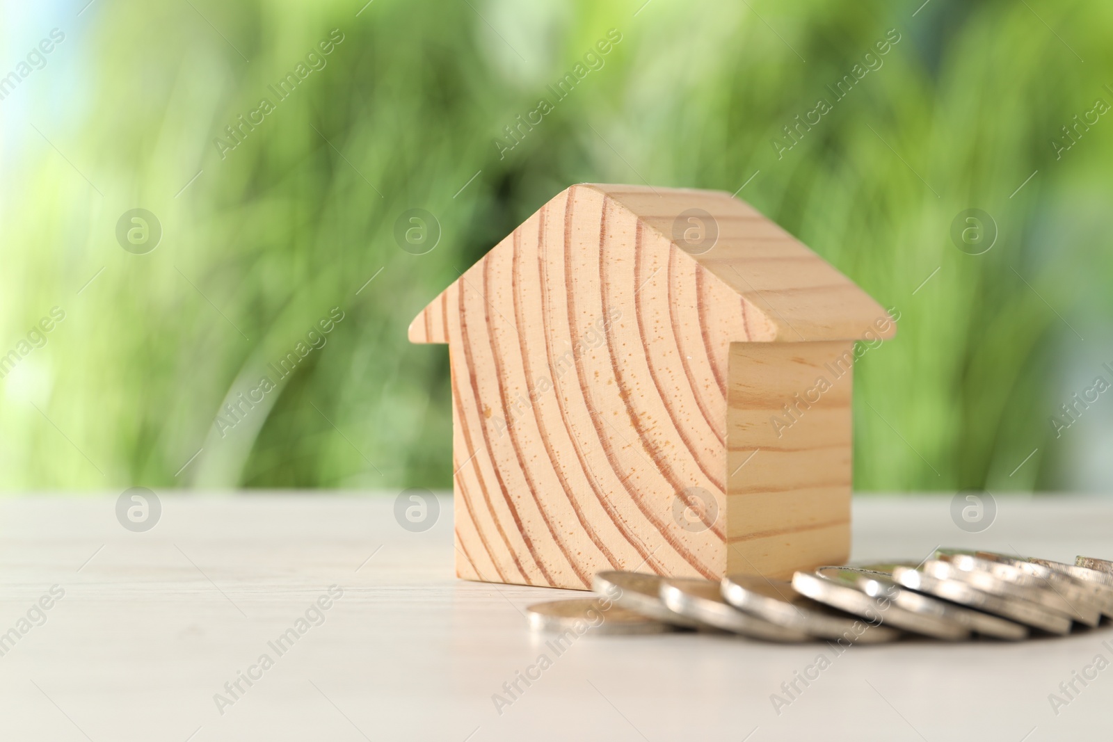 Photo of Wooden house model and coins on light table outdoors, space for text