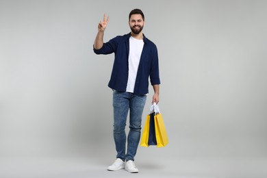 Photo of Happy man with many paper shopping bags showing peace sign on grey background
