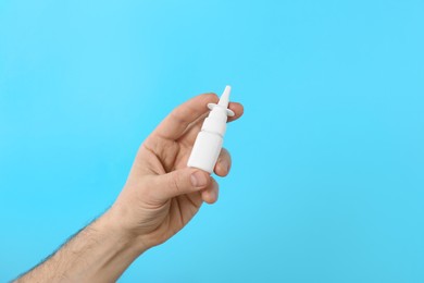 Photo of Man holding nasal spray on light blue background, closeup. Space for text