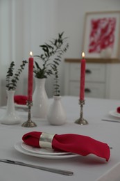 Table setting. Plates, pink napkin, cutlery, burning candles and vases with green branches in dining room