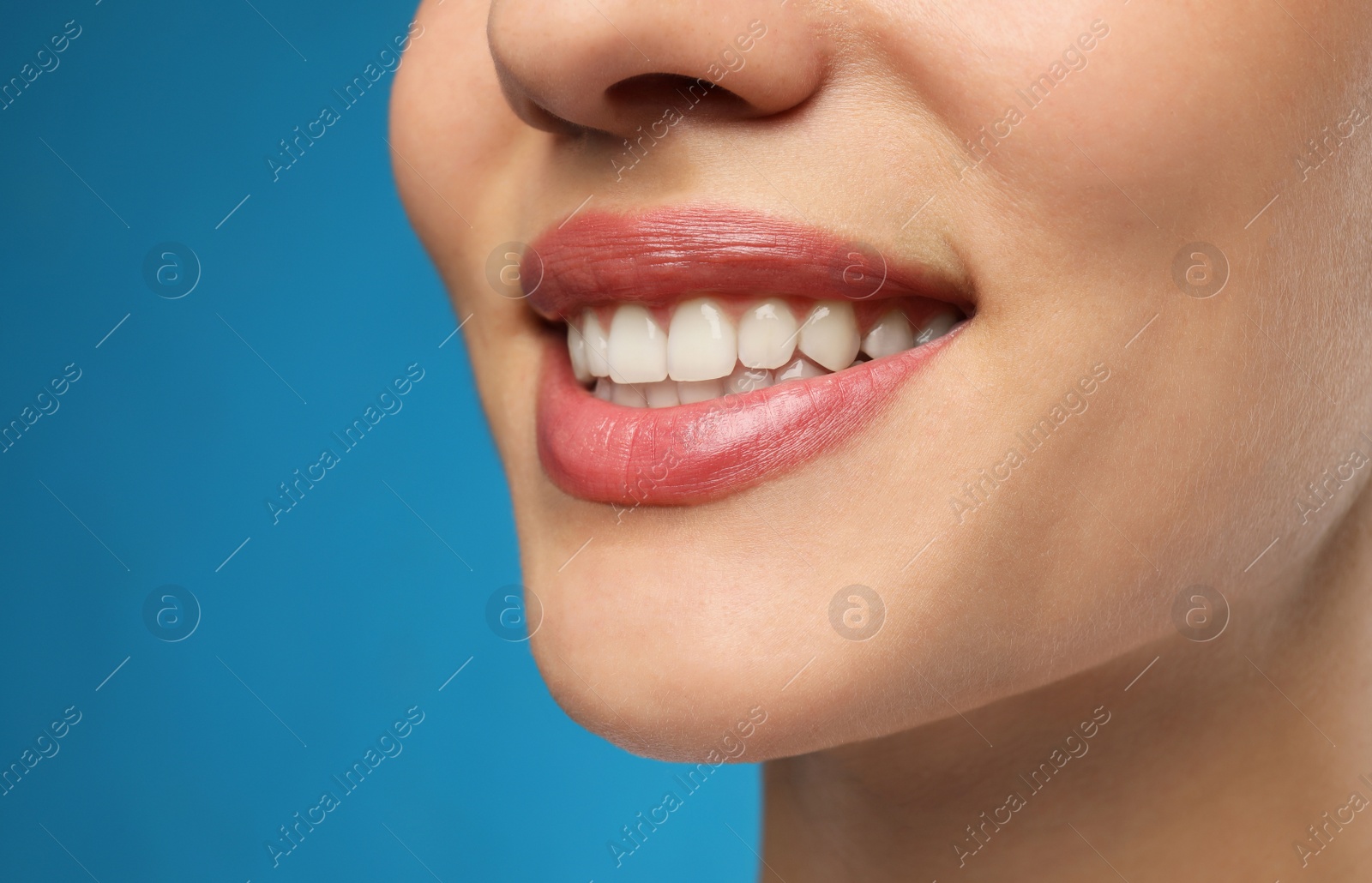 Photo of Woman with healthy teeth and beautiful smile on blue background, closeup. Cosmetic dentistry