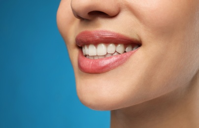 Photo of Woman with healthy teeth and beautiful smile on blue background, closeup. Cosmetic dentistry