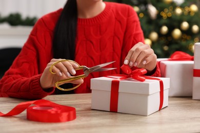 Photo of Woman decorating Christmas gift box at wooden table indoors, closeup