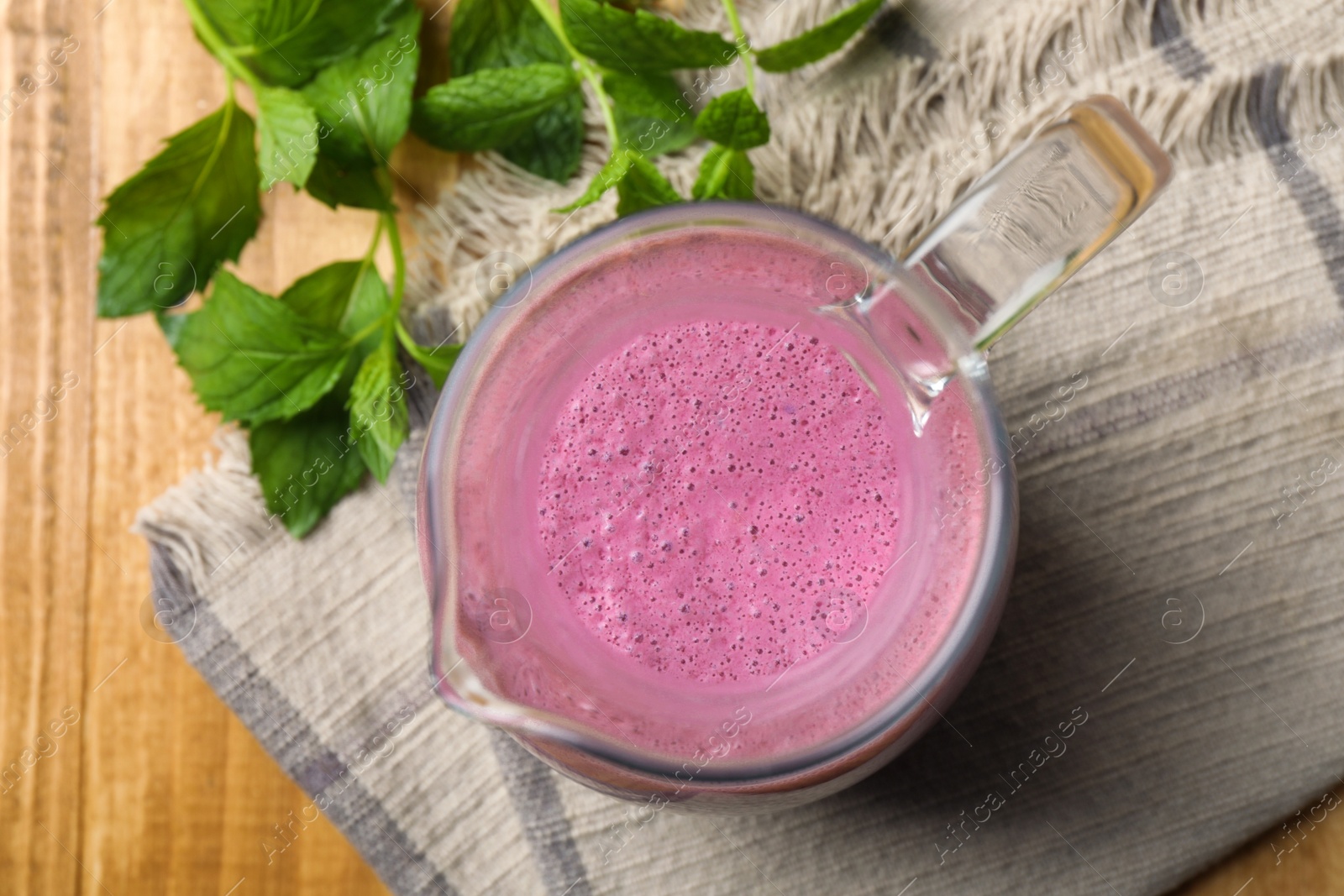 Photo of Glass jug of blackberry smoothie and mint on wooden table, flat lay