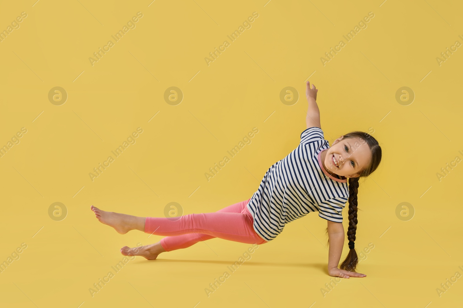 Photo of Cute little girl doing gymnastic exercise on yellow background