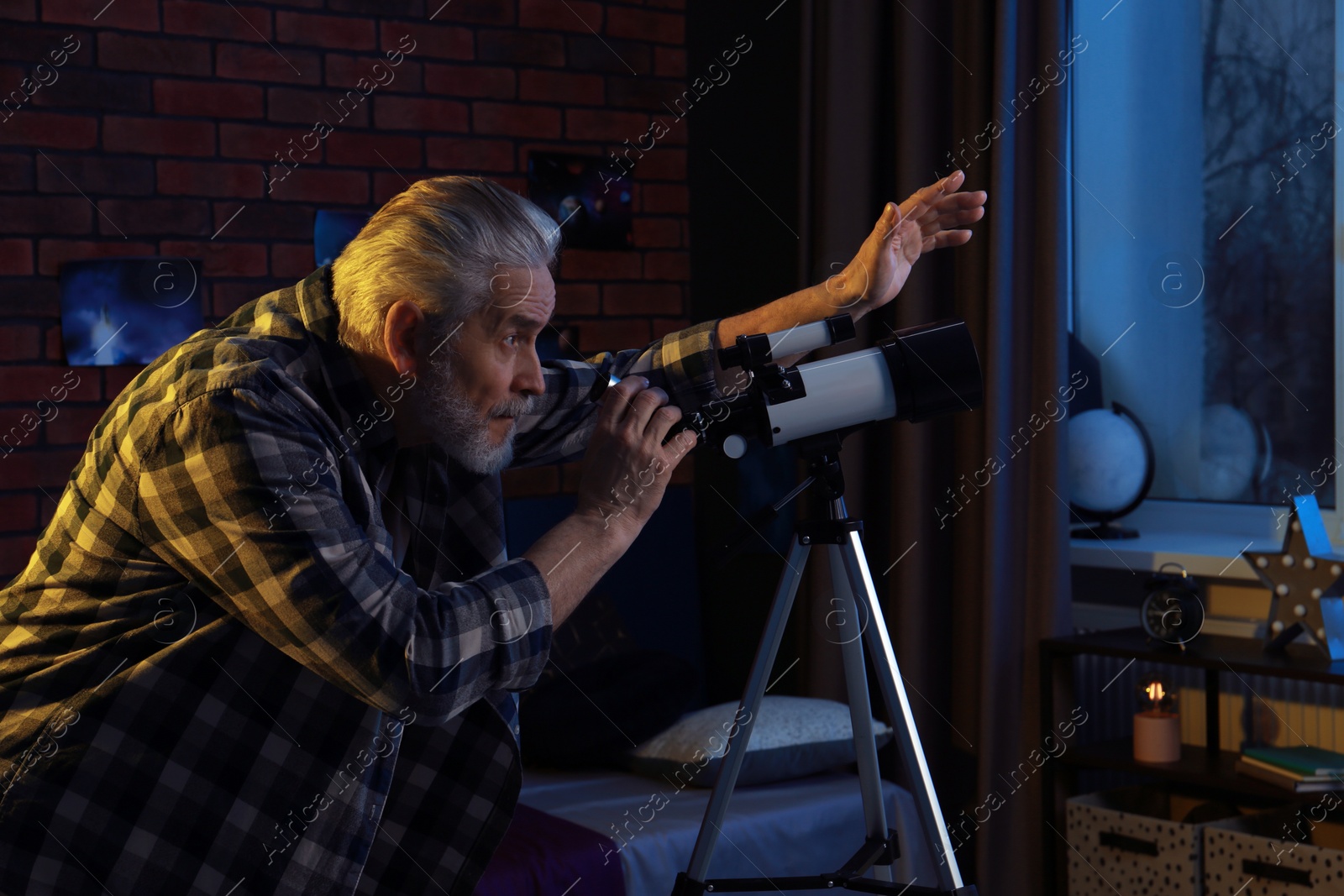 Photo of Senior man looking at stars through telescope in room