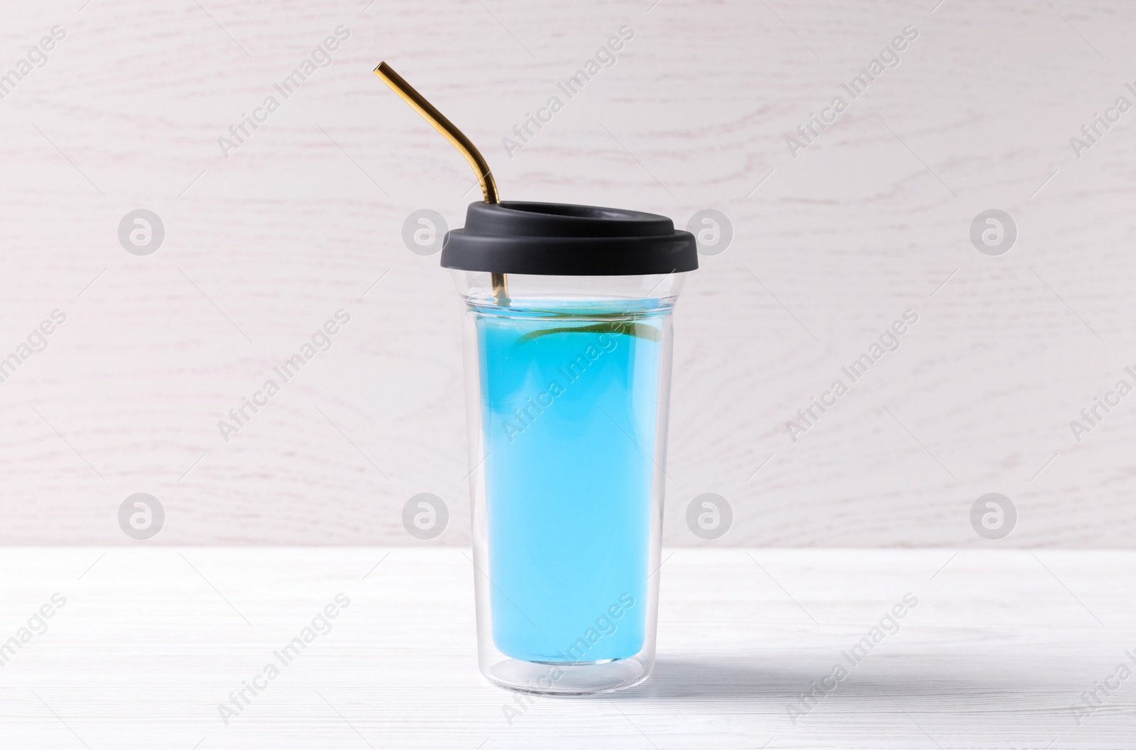 Photo of Bright light blue drink in glass with lid and straw on white wooden table