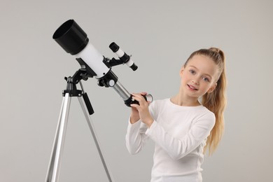 Happy little girl with telescope on light grey background