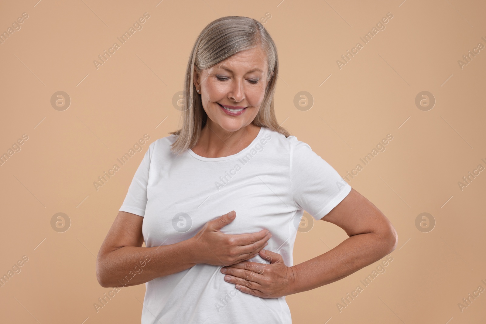 Photo of Smiling senior woman doing breast self-examination on light brown background