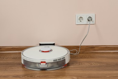 Robotic vacuum cleaner charging on wooden floor indoors