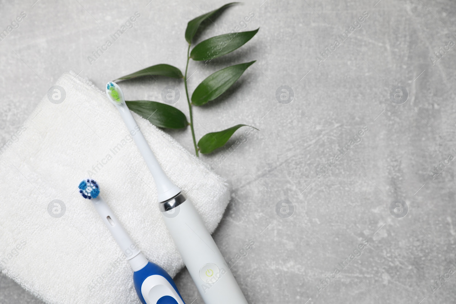 Photo of Electric toothbrushes, towel and leaves on grey textured table, flat lay. Space for text