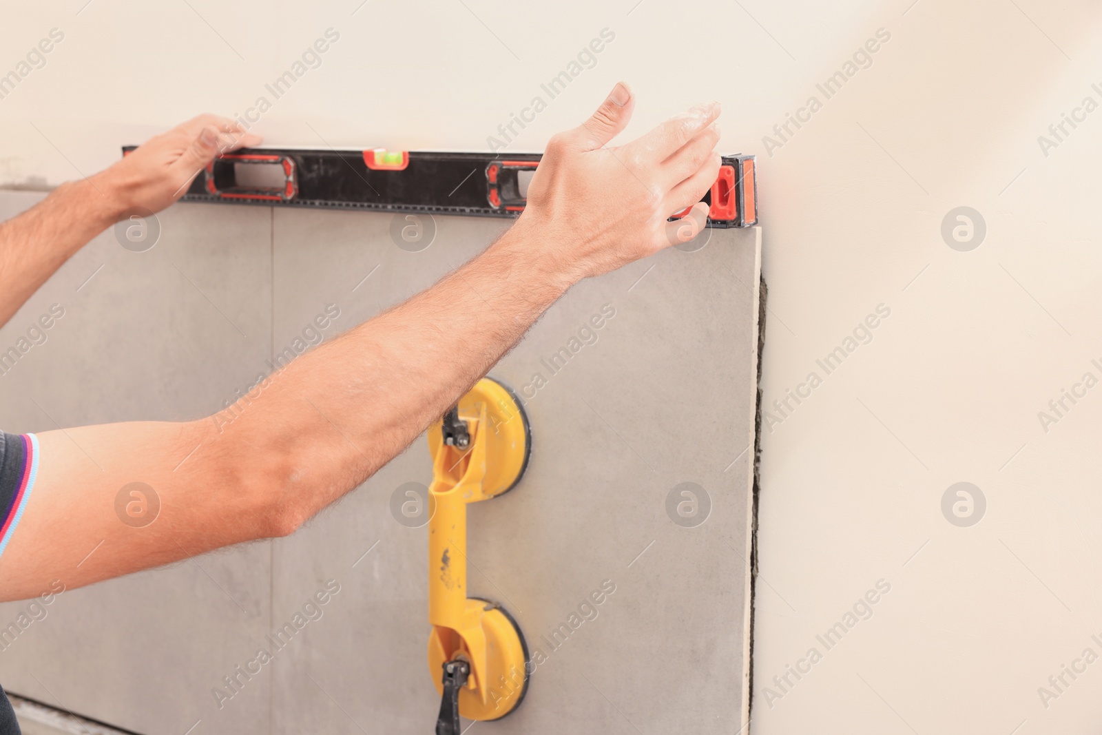 Photo of Worker using building level for tiles installation on wall indoors, closeup