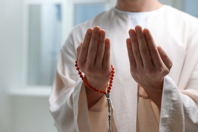 Photo of Muslim man with misbaha praying near window indoors, closeup. Space for text