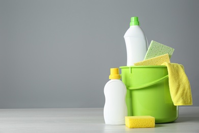 Photo of Bucket with cleaning products and sponges on grey table. Space for text