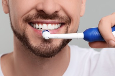 Photo of Man brushing his teeth with electric toothbrush on light grey background, closeup