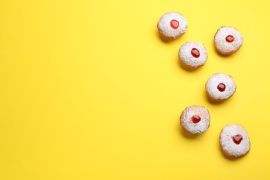 Photo of Hanukkah donuts with jelly and powdered sugar on yellow background, flat lay. Space for text