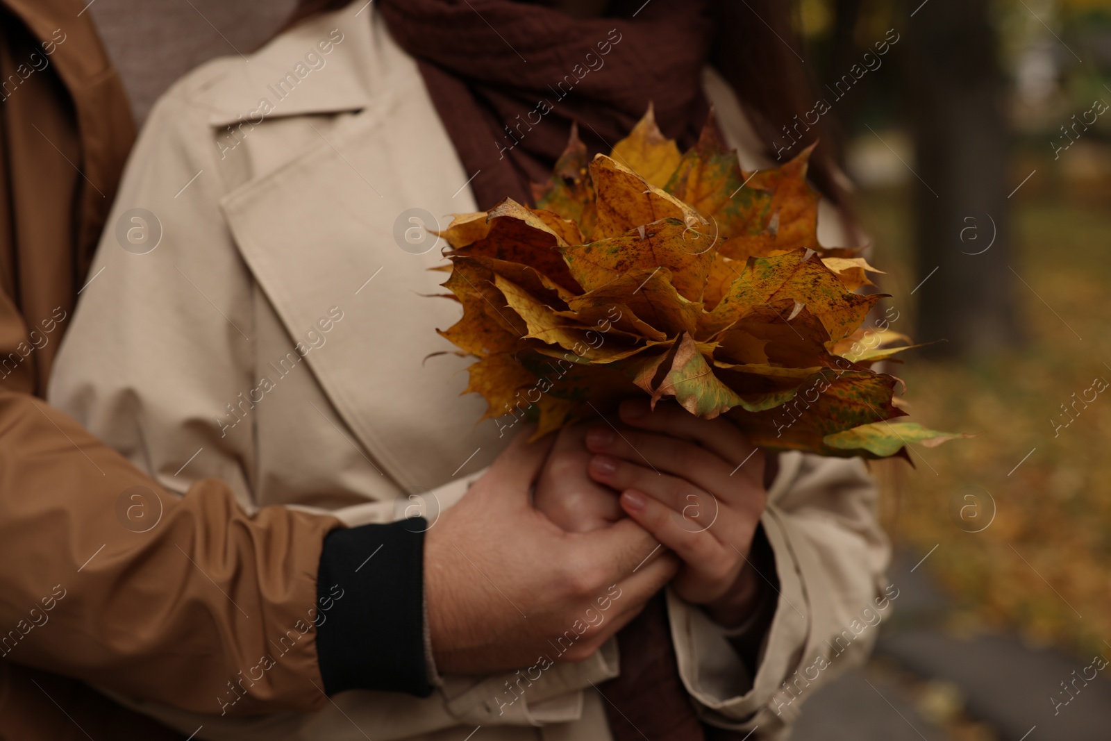 Photo of Happy young couple with dry leaves in autumn park, closeup