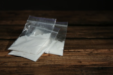 Cocaine in plastic bags on wooden background. Space for text