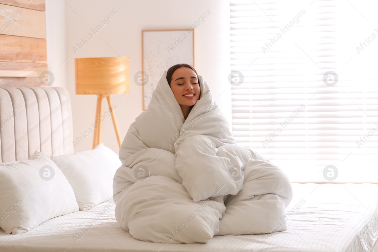 Photo of Beautiful young woman wrapped with soft blanket on bed at home