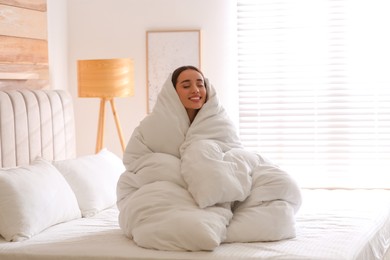 Photo of Beautiful young woman wrapped with soft blanket on bed at home