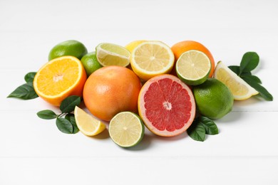 Photo of Different fresh citrus fruits and leaves on white wooden table