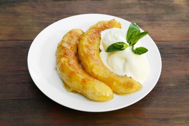 Photo of Plate with delicious fried bananas, ice cream and mint leaves on wooden table
