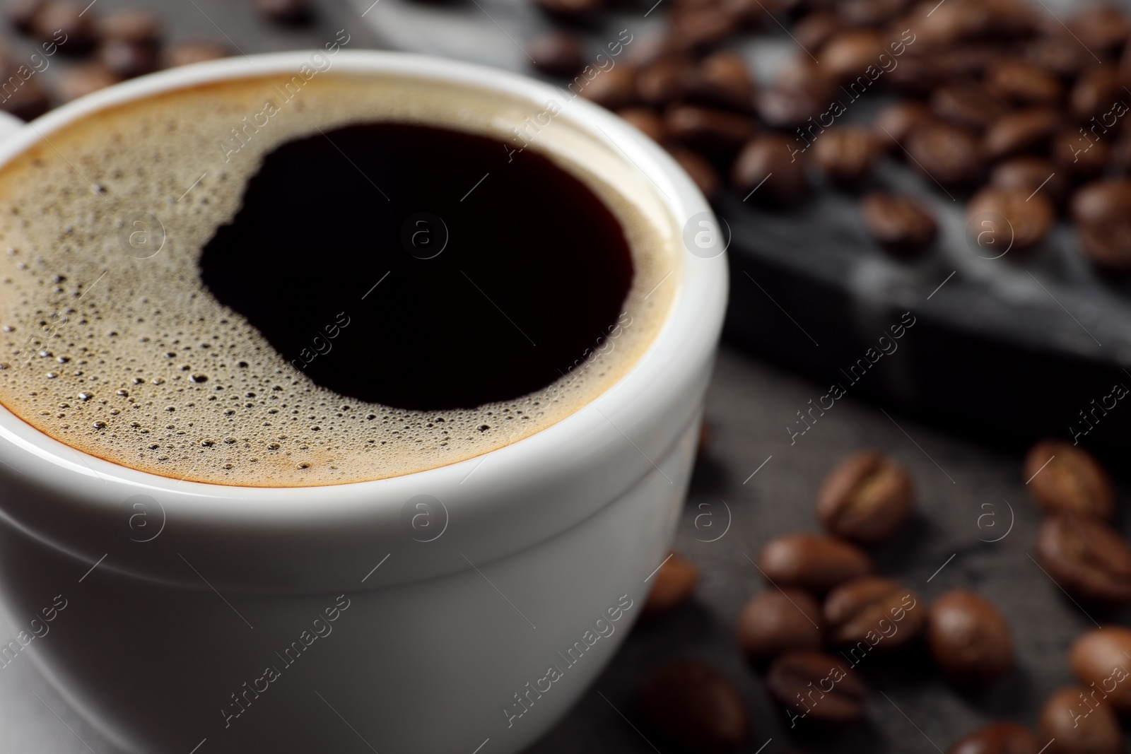 Photo of Cup of aromatic hot coffee and beans on grey table, closeup. Space for text